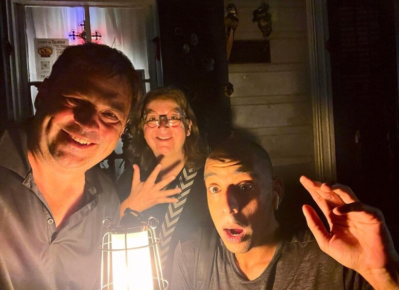 Three people posing indoors with a lantern and a sign in the background. 4