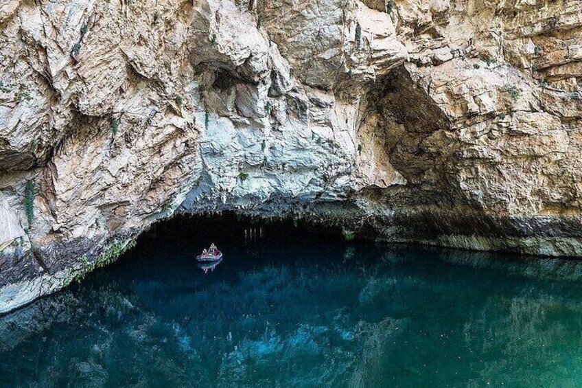 A rocky cave entrance with clear water and a boat in the distance. 4