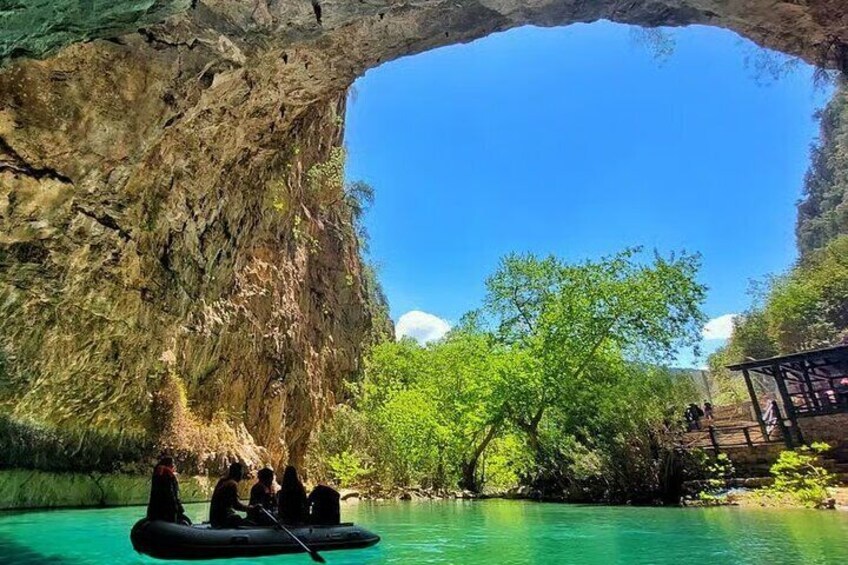 A group of people on a raft in a turquoise river under a large rock arch. 3