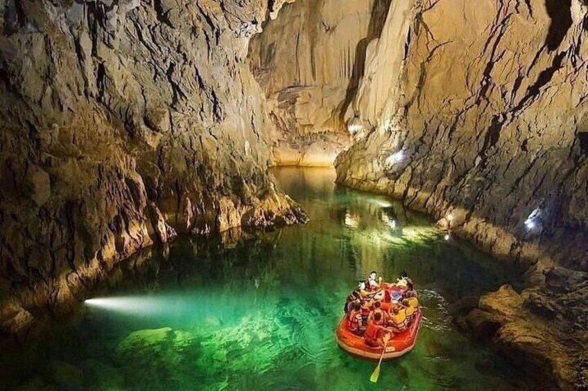 A cave with a clear water pool and a red raft with people. 5