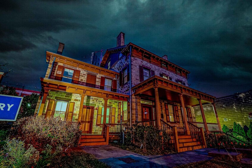 A multi-story building with illuminated windows and a porch, set against a dark, cloudy sky. 2