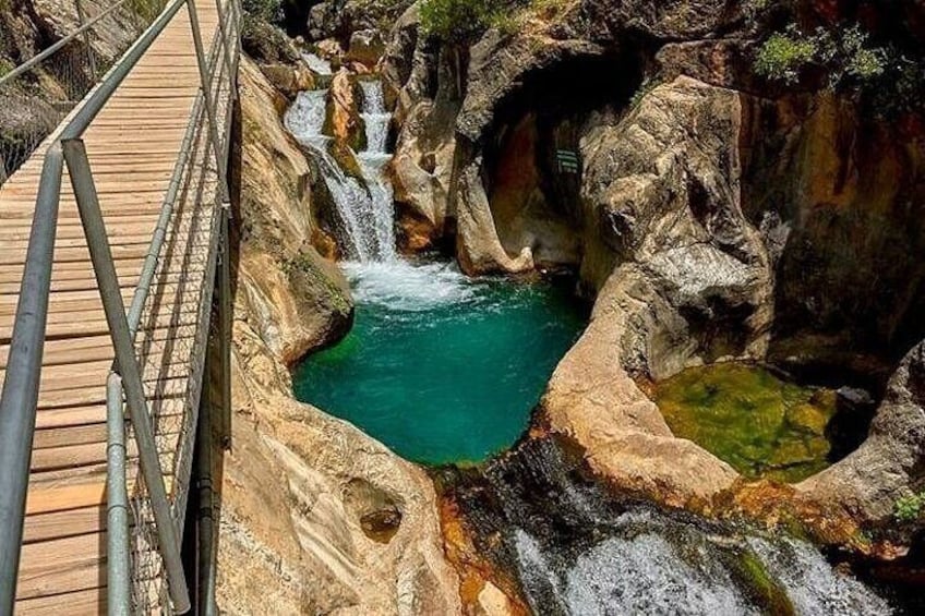 A wooden bridge over a turquoise pool with waterfalls. 2