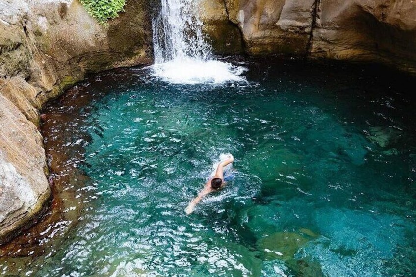 A person swimming in a clear blue pool with a waterfall above. 4