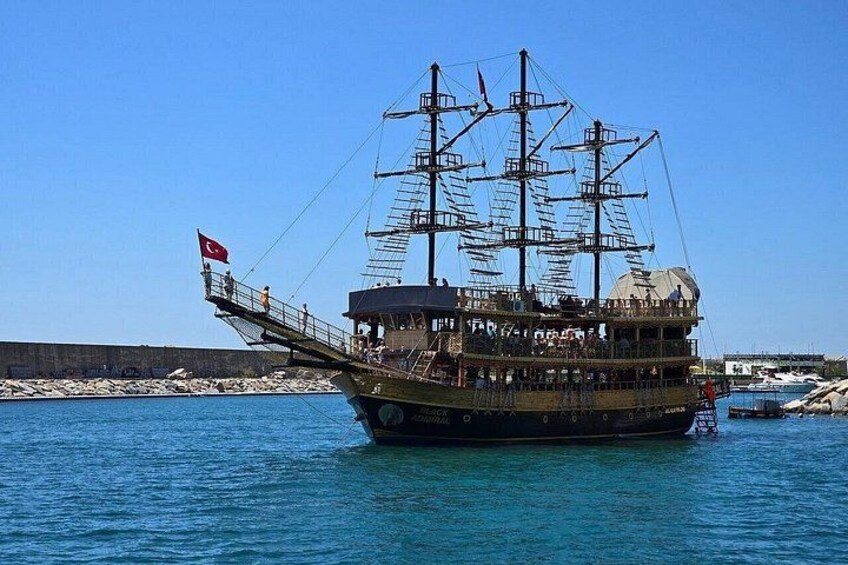 Un grand navire à plusieurs ponts et doté de nombreux mâts, ancré dans un port aux eaux d’un bleu limpide et aux rivages rocheux. 1