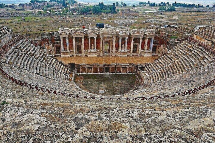An ancient amphitheater with a central stage and tiered seating. 3