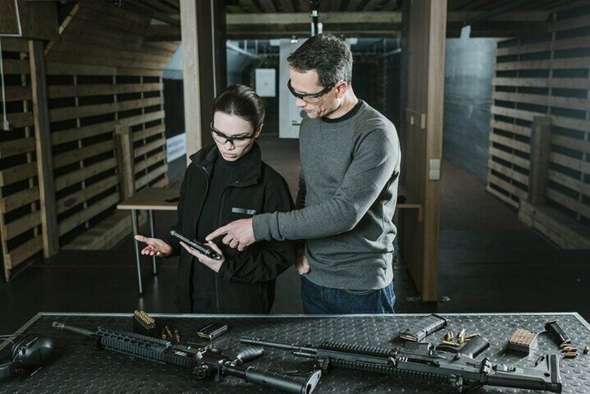 Two people examining a firearm on a table in a warehouse with shelves in the background. 2
