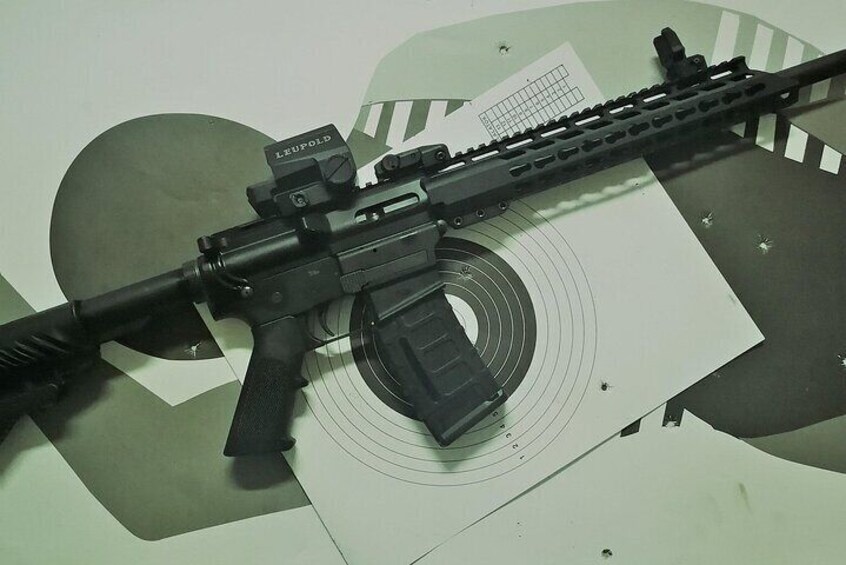 A firearm with a scope and a magazine lying on a surface with a target in the background. 4
