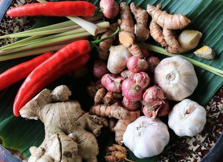 A variety of fresh vegetables including red chili peppers, ginger, onions, and garlic laid out on a banana leaf. 2