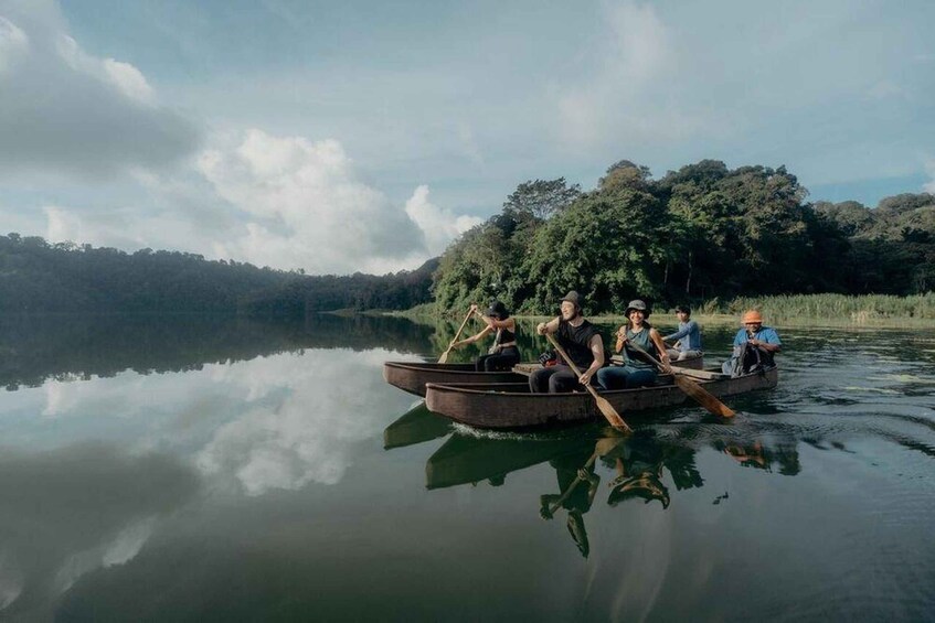 A group of people rowing a boat on a calm lake surrounded by dense forest. 1