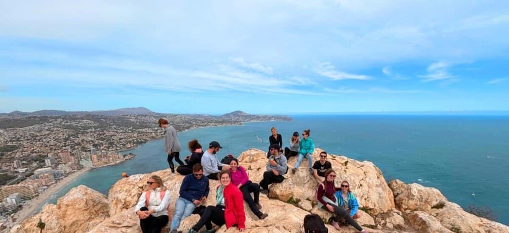 A group of people on a rocky outcrop overlooking a coastal city and the sea. 1