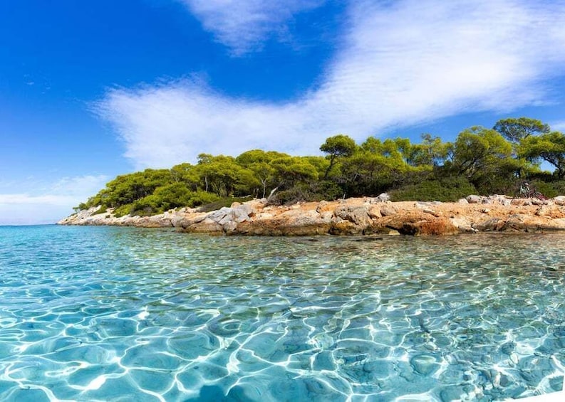 A clear turquoise sea, rocky shoreline, and dense green trees. 1