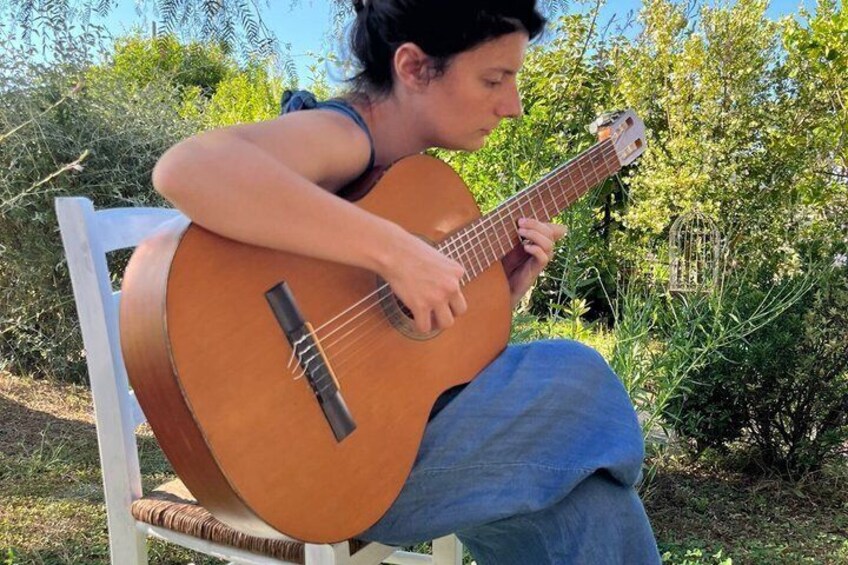 A person playing a guitar on a white chair outdoors. 1