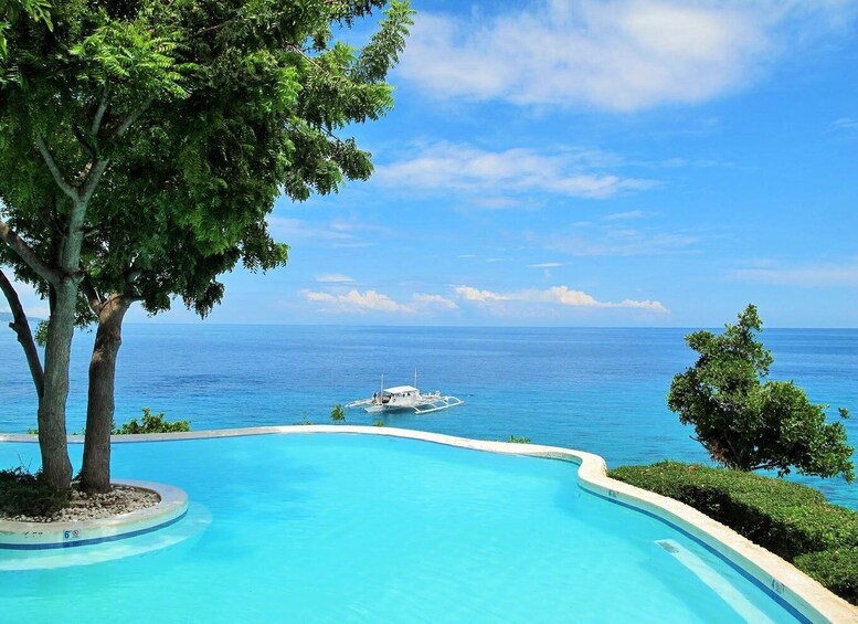 A clear blue pool with a view of the ocean and a boat in the distance. 3
