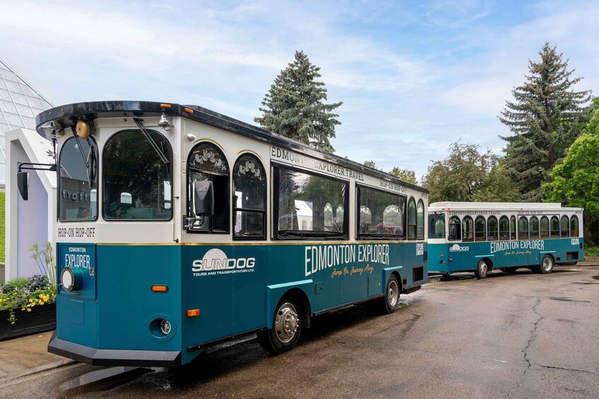Two Edmonton Explorer buses parked in a lot with trees and a building in the background. 1