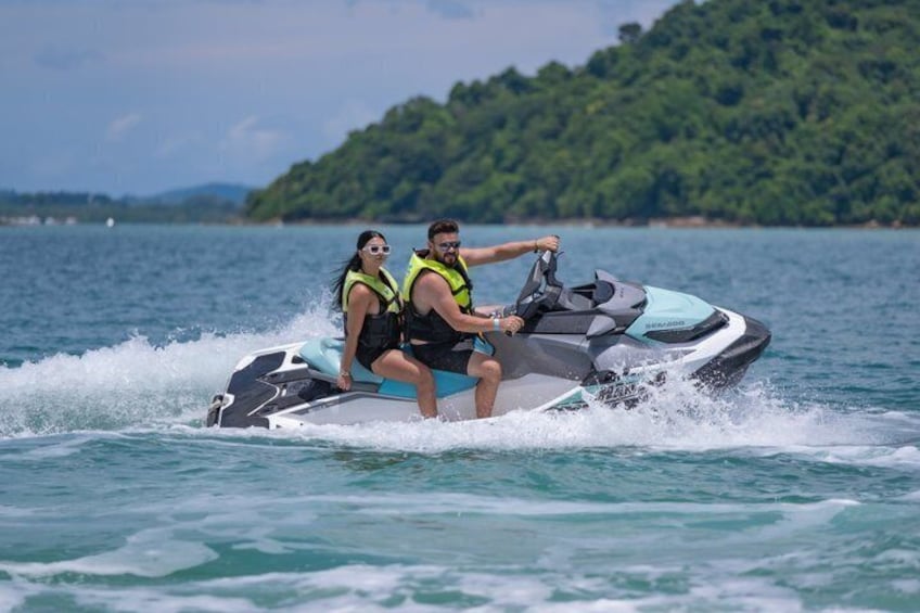Two people on a jet ski with a forested island in the background. 1