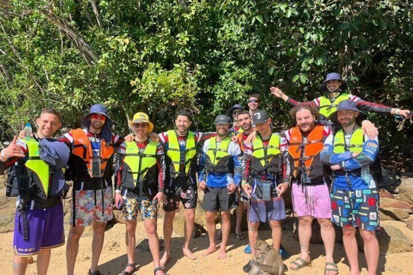 A group of people wearing life jackets and holding paddles, standing on a sandy beach with trees in the background. 2
