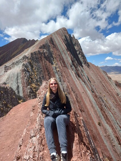 A person sitting on a rocky outcrop with a mountain in the background. 5