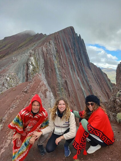 Three people posing in front of a mountain with red and green rock formations. 3