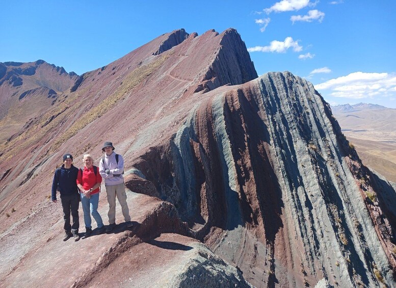 Three people standing on a rocky mountain ridge with a clear sky. 5