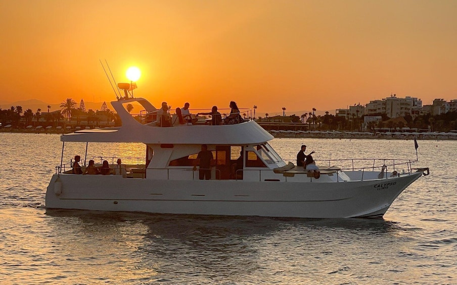 A boat with passengers at sunset, water, and a distant shoreline with buildings. 1