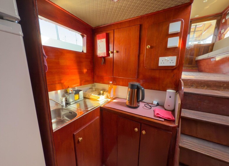 A compact kitchen with wooden cabinets, a stainless steel sink, a kettle, and a toaster. 2