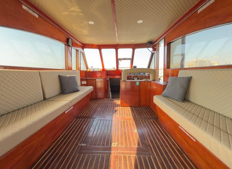 A boat's interior with wooden flooring, cushioned seating, and a steering wheel. 5