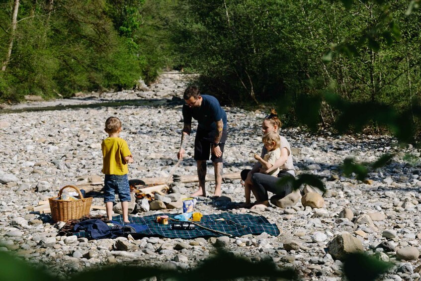 A family camping by a river with a picnic setup on the ground. 2