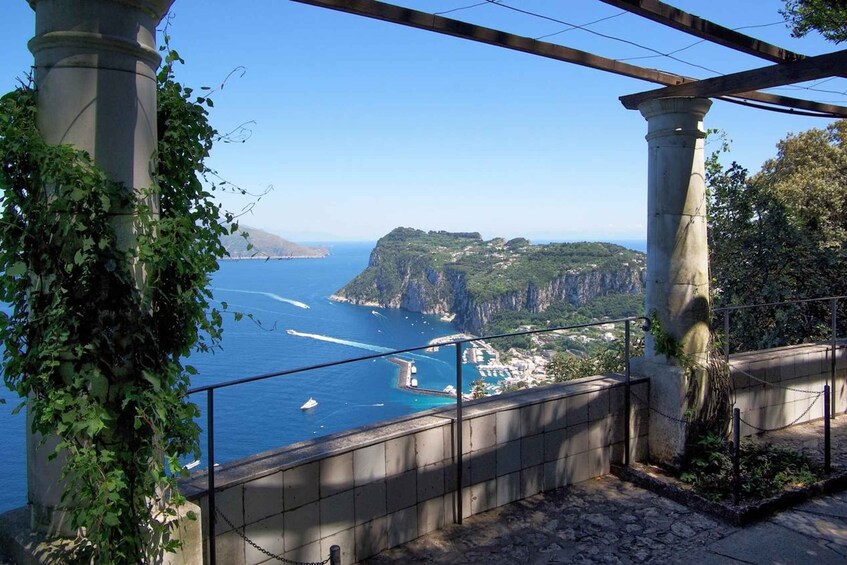 A coastal view with a stone staircase, a railing, and a clear blue sea. 1
