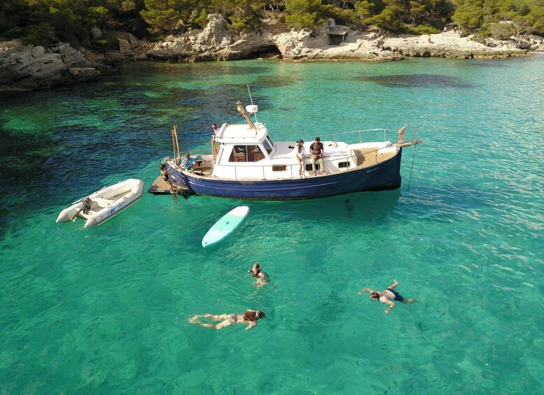 A boat anchored in clear turquoise water with people swimming and a smaller boat nearby. 2