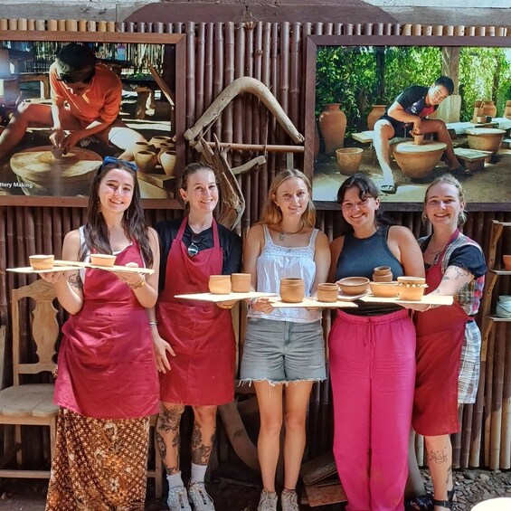 A group of people in aprons holding trays of pottery at a workshop. 4
