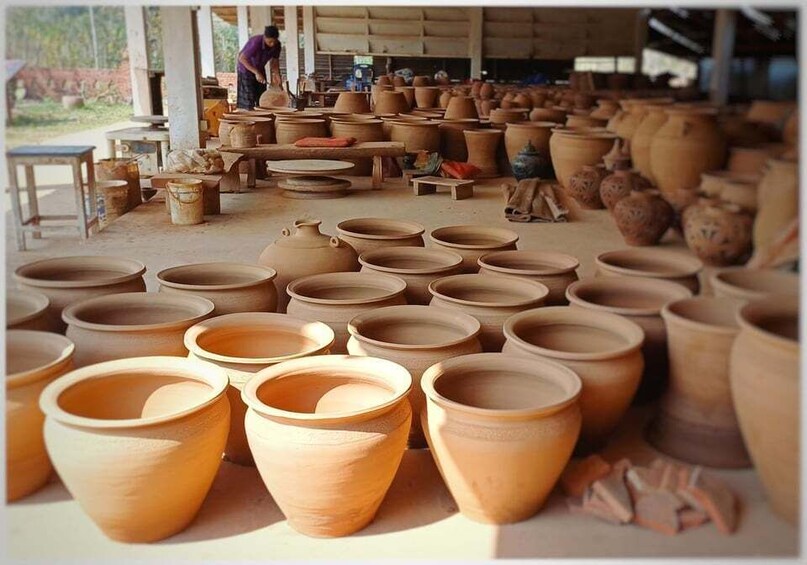 A pottery workshop with numerous clay pots and a person working in the background. 5