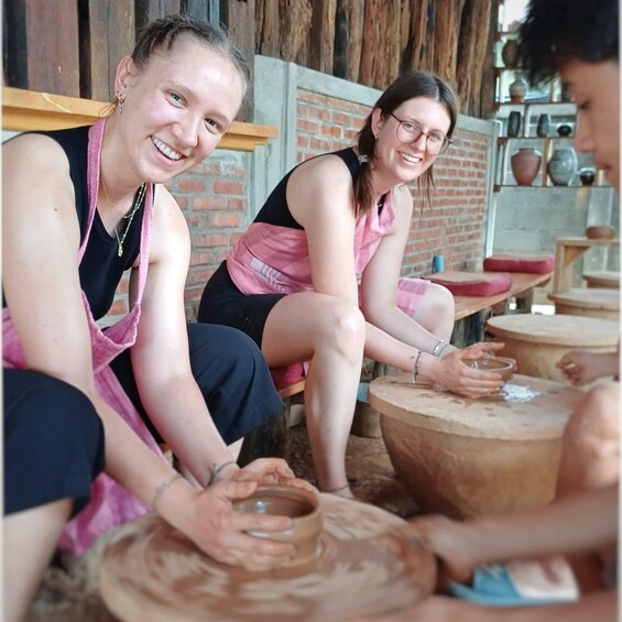 Three individuals engaged in pottery making, seated at a table with clay and pottery wheels. 1