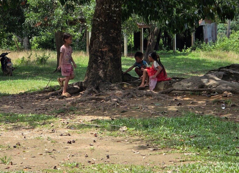 Children playing near a tree in a grassy area with a motorcycle in the background. 5