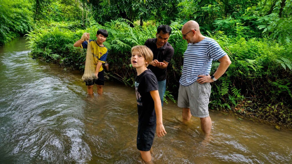 A group of people wading through a shallow river surrounded by dense greenery. 5