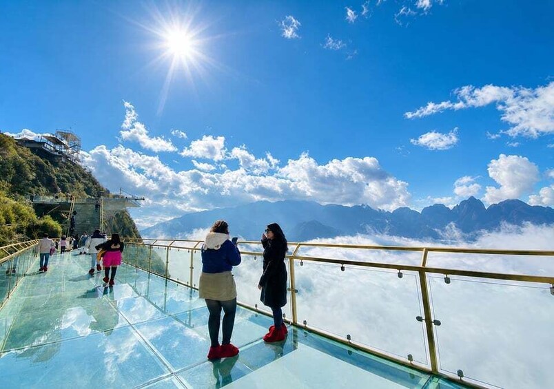 A glass bridge with people walking on it, overlooking a mountain range. 4