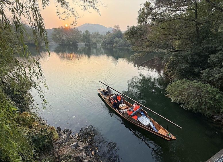 A wooden boat on a calm river surrounded by dense foliage and hills in the background. 1