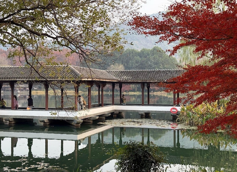 A traditional pavilion over a calm pond with people walking around. 4