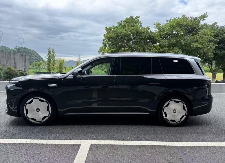 A black station wagon parked on a road with trees and a cloudy sky in the background. 4