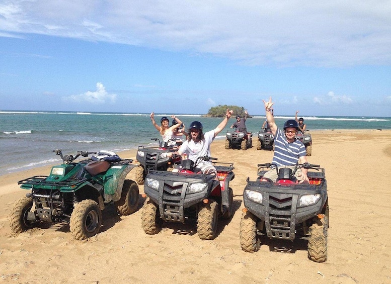 Four people on ATVs on a sandy beach with the ocean in the background. 5