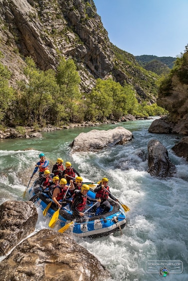 A group of people in a blue raft navigating a river with rocks and rapids. 2