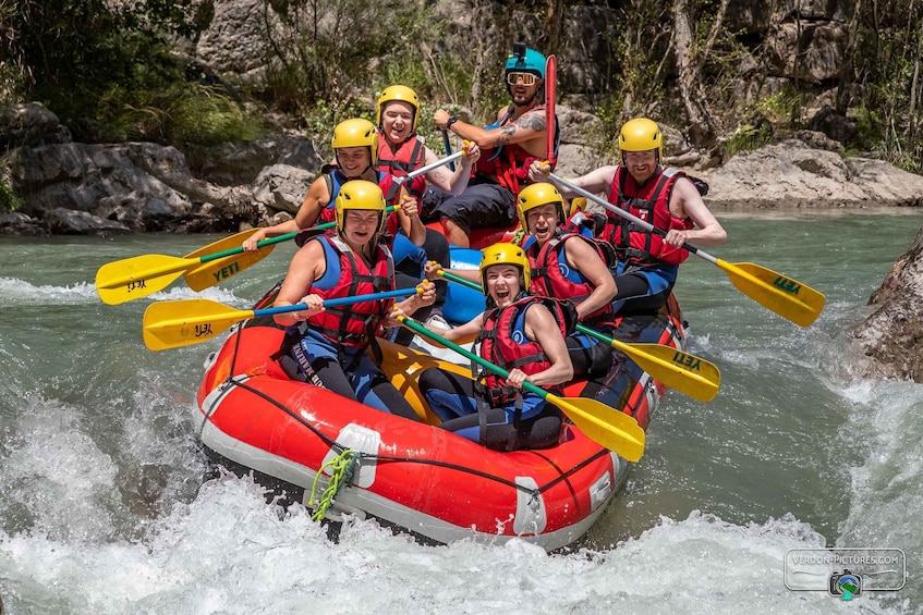 A group of people in a red inflatable raft paddling on a river surrounded by rocky terrain. 3