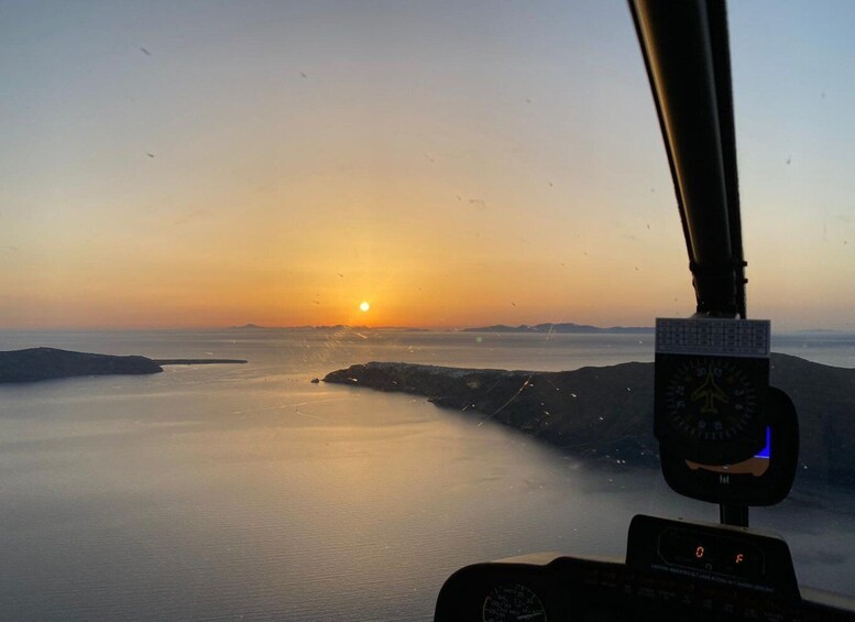 A helicopter cockpit with a view of a sunset over a calm sea and distant land. 3
