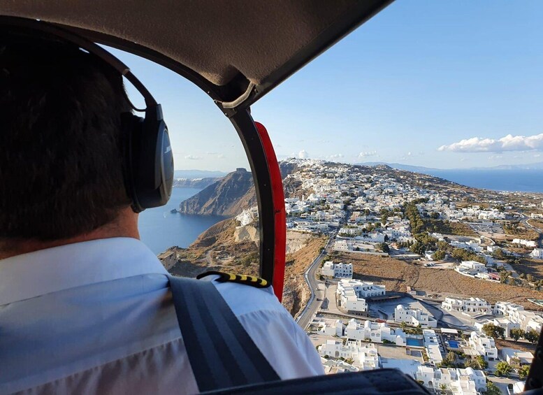 A pilot's view from a helicopter, overlooking a coastal town with white buildings and a mountainous backdrop. 5