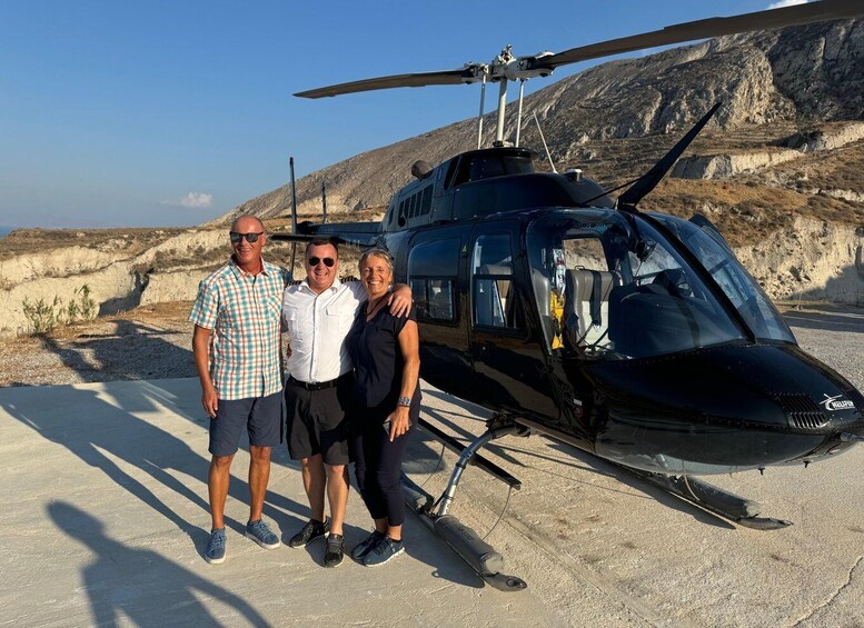 Three people standing in front of a black helicopter with a mountainous background. 4
