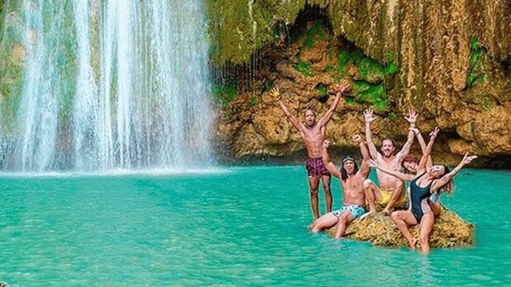 A group of people enjoying a natural water setting with a waterfall and rocky cliffs. 2