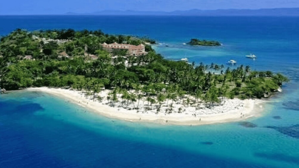 An island with a beach, clear blue waters, and a building on the shore. 1
