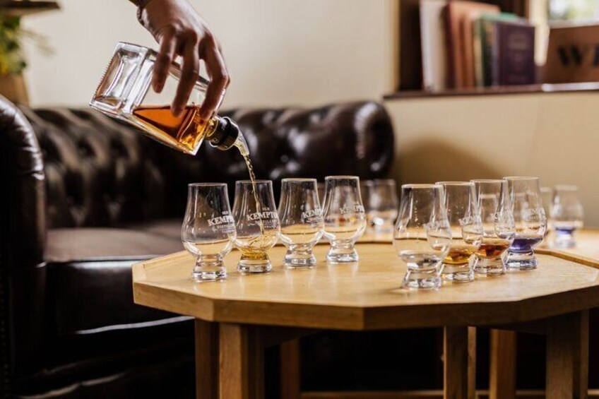 A hand pouring a liquid into several glasses on a wooden table. 4