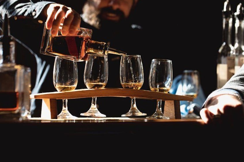 A person pouring a liquid into a series of glasses on a wooden stand. 1