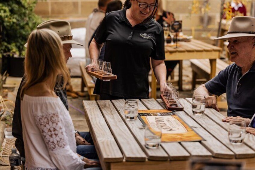 A person serving drinks at an outdoor wooden table with a menu. 2