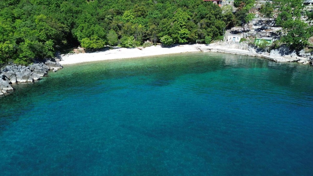 A clear turquoise bay with white sand, surrounded by dense green forest and rocky outcrops. 4